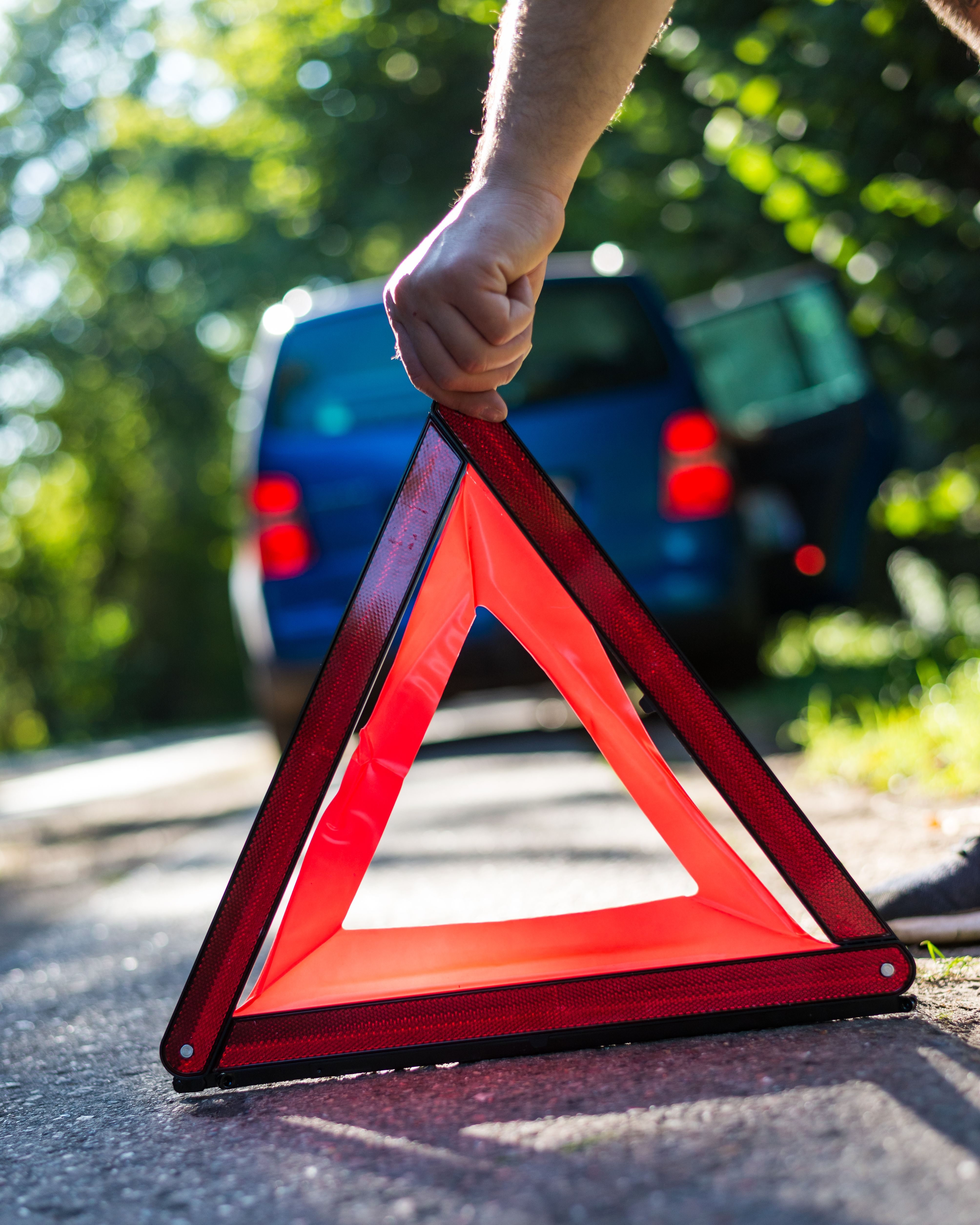 Hand placing an emergency warning triangle beside a broken-down vehicle for roadside safety
