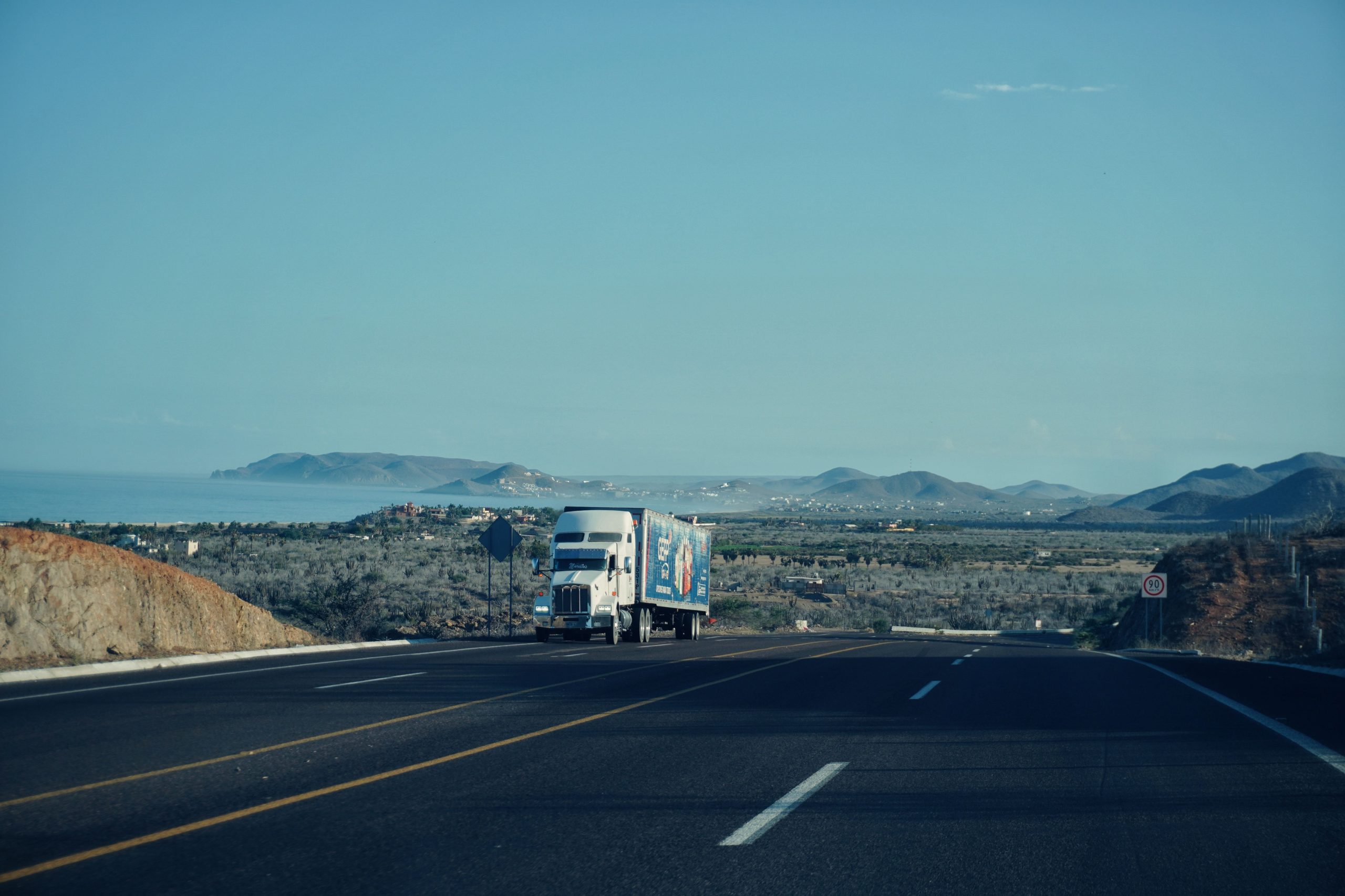 Semi-truck traveling on a scenic highway with mountains in the background, representing long-haul trucking routes