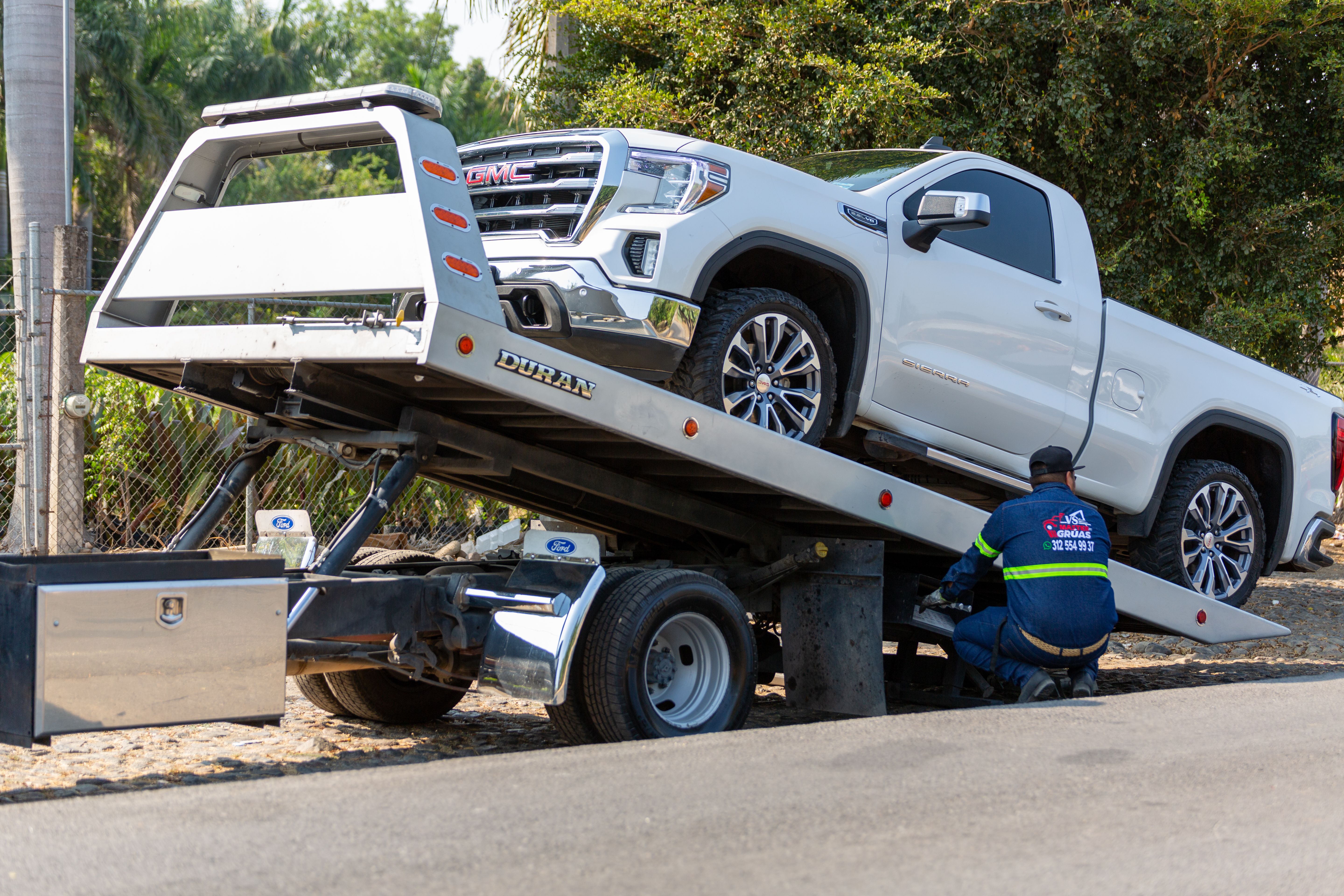 Tow truck operator loading a broken-down pickup truck onto a flatbed for towing