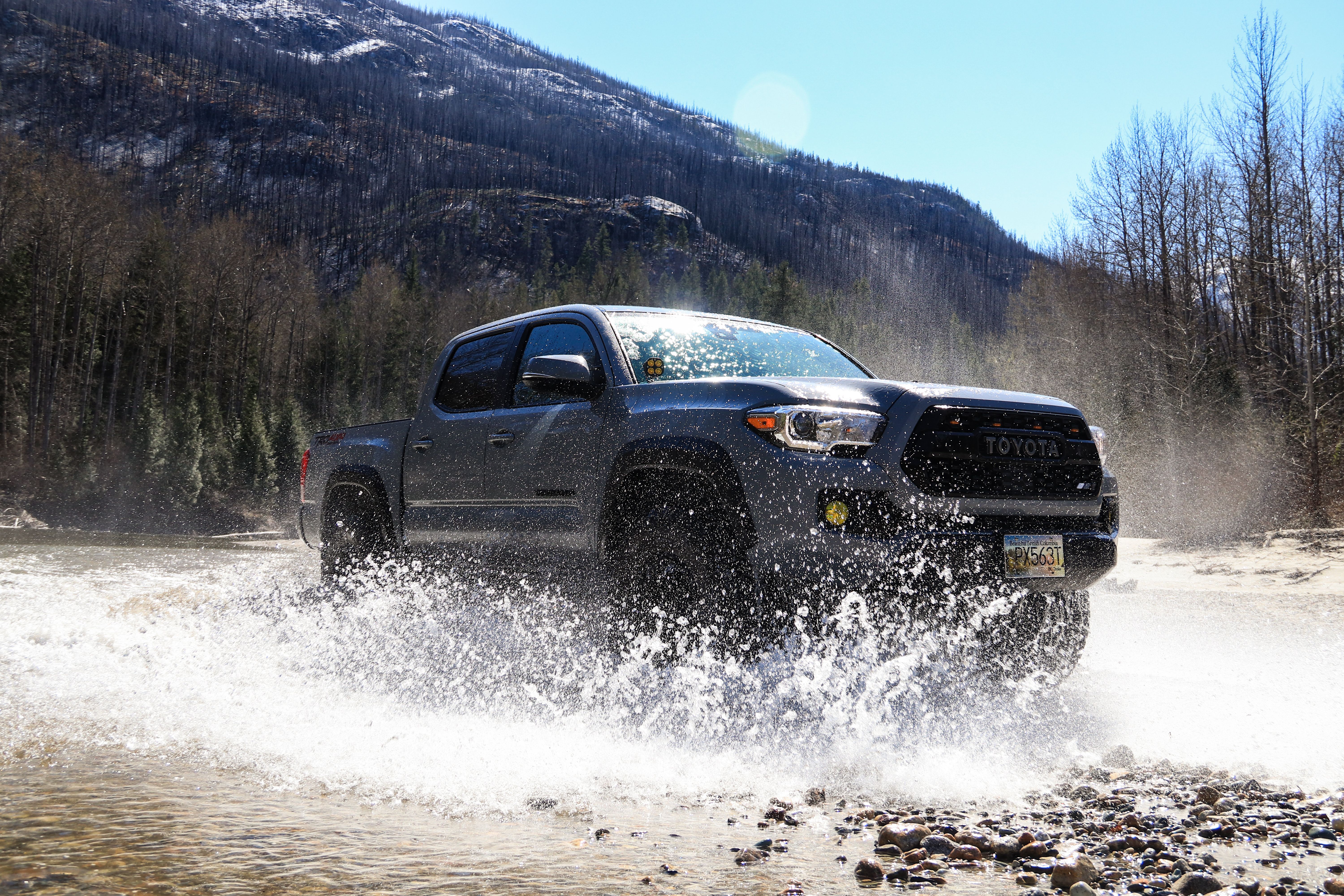 Toyota Tacoma driving through a puddle in a rugged setting, illustrating capability in demanding conditions.